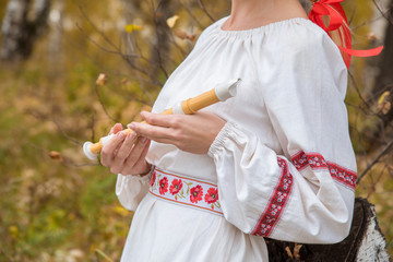 The girl in the Slavic dress holds in her hands a flute in the autumn forest
