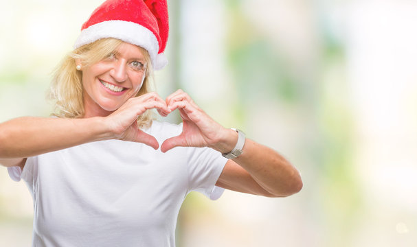 Middle age blonde woman wearing christmas hat over isolated background smiling in love showing heart symbol and shape with hands. Romantic concept.