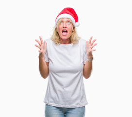 Fototapeta na wymiar Middle age blonde woman wearing christmas hat over isolated background crazy and mad shouting and yelling with aggressive expression and arms raised. Frustration concept.