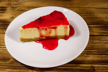 Piece of tasty New York cheesecake with raspberry jam in a white plate on wooden table