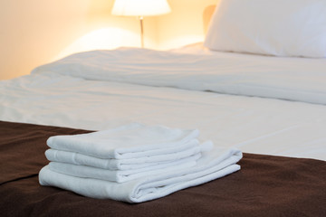 Fototapeta na wymiar White folded towels, linen beddings on tidy bed.