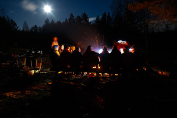 People sit at night round bright bonfire