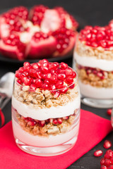 Pomegranate parfait - sweet organic layered dessert with granola flakes, yogurt and fruit seeds on black background.
