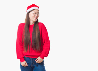 Young Chinese woman over isolated background wearing christmas hat looking away to side with smile on face, natural expression. Laughing confident.