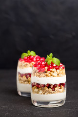 Pomegranate parfait - sweet organic layered dessert with granola flakes, yogurt and fruit seeds on black background.
