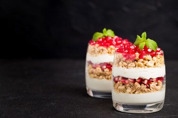 Pomegranate parfait - sweet organic layered dessert with granola flakes, yogurt and fruit seeds on black background.