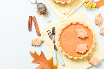 Fototapeta na wymiar Pumpkin pie with cinnamon and cookies on yellow napkins on pastel blue background with autumn yellow leaves.
