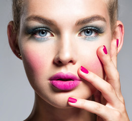 Beautiful woman face with blue makeup of eyes and pink nails.