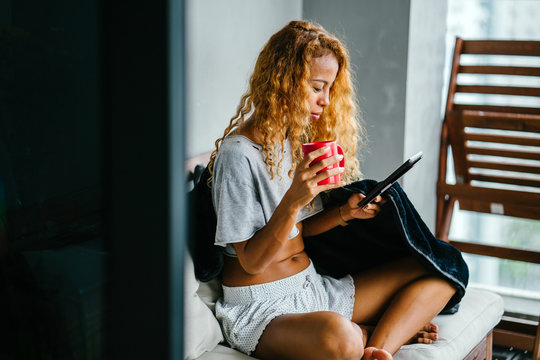 Portrait of a tanned and sexy Indonesian woman sipping from a hot mug of tea during the day on a weekend. She is comfortable and relaxed on the balcony of her apartment.