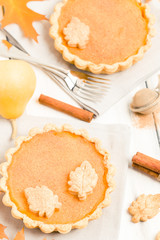Pumpkin pie with cinnamon and cookies on gray napkins on white wooden background with autumn yellow leaves.