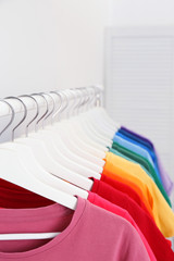 Rack with bright clothes in room. Rainbow colors