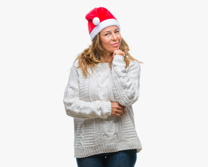 Middle age senior hispanic woman wearing christmas hat over isolated background with hand on chin thinking about question, pensive expression. Smiling with thoughtful face. Doubt concept.