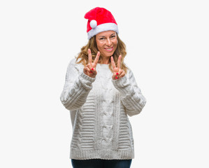 Middle age senior hispanic woman wearing christmas hat over isolated background smiling looking to the camera showing fingers doing victory sign. Number two.
