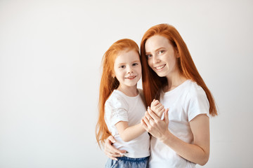 Close-up portrait of smiling mother hugging cute four year old daughter isolated on white...