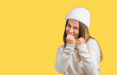 Beautiful middle age woman wearing winter sweater and hat over isolated background Ready to fight with fist defense gesture, angry and upset face, afraid of problem