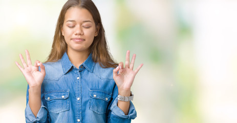 Young beautiful brunette woman wearing blue denim shirt over isolated background relax and smiling with eyes closed doing meditation gesture with fingers. Yoga concept.