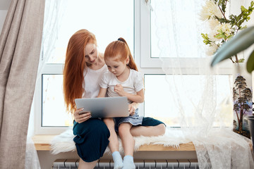 Happy redheaded mother and daughter spending time together , Mom helps her sweety to do homework...