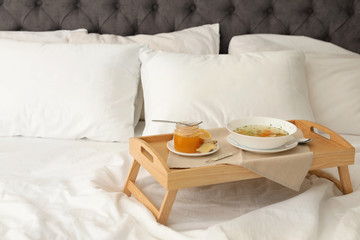Tray with bowl of fresh homemade soup to cure flu on bed