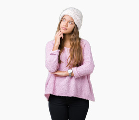 Young beautiful brunette woman wearing sweater and winter hat over isolated background with hand on chin thinking about question, pensive expression. Smiling with thoughtful face. Doubt concept.