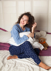 Young beautiful woman sitting on bed and smiling with pillow