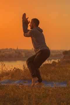 Man doing yoga on sunset with city view,Garudasana/Eagle Pose.Toned image.