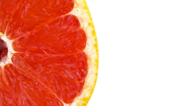 View from above. Half frame of a pink grapefruit cross section cut. Vertically rotating on the turntable. Isolated on the white background. Close-up. Macro.
