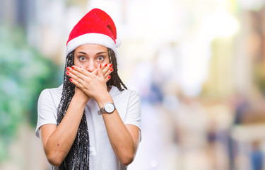 Young braided hair african american girl wearing christmas hat over isolated background shocked covering mouth with hands for mistake. Secret concept.