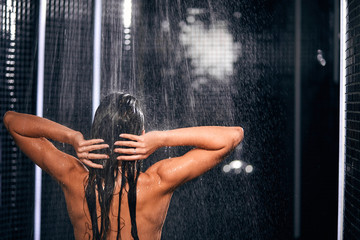 Rear view of slim fit woman in the shower, washing under refreshing water, standing in shower room after intense workout, healthy lifestyle, enjoying time in luxury spa resort