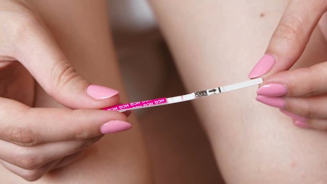 Woman makes a pregnancy test. Waiting for the result, looking at the test strip. Close-up hands and legs.