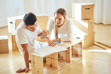 couple reads instructions for Assembly of furniture in new house with moving boxes on background