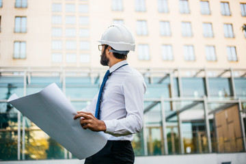 Young architect at work with helmet and plans for the project in hand