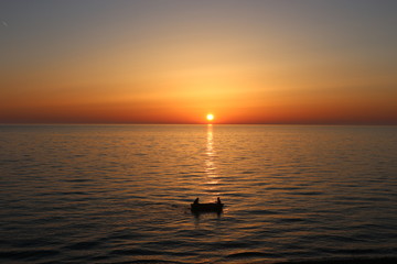 Two friends inside a silhouetted boat moving slowly against a colorful sunset in the coast of Kobuleti in the Georgian coast of the Black Sea