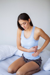 Stomach Pain. Unhealthy young woman with stomachache leaning on the bed at home