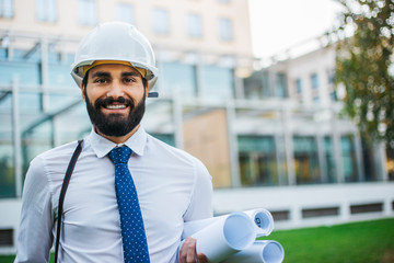 Young architect at work with helmet and plans for the project in hand