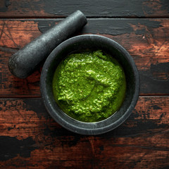 Green Basil Pesto in marble mortar with parmesan cheese, pine nuts, garlic and lemon on wooden rustic background