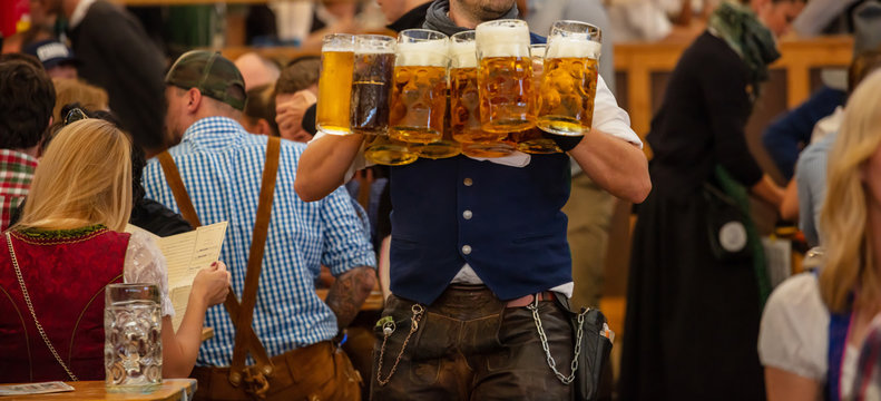 Oktoberfest, Munich, Germany. Waiter serve beer, closeup view. People in traditional Bavarian costume 