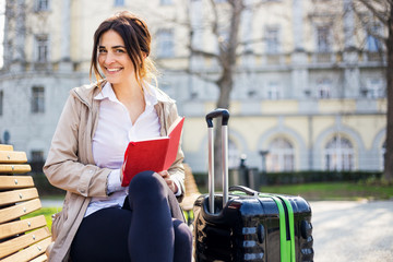 Traveling business woman sitting on the banch with bag and working on laptop