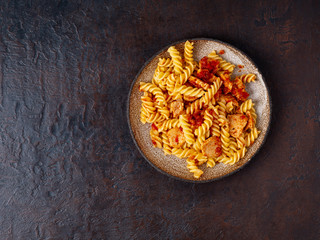fusilli pasta with tomato sauce, chicken fillet on dark stone concrete background, copy space, top view