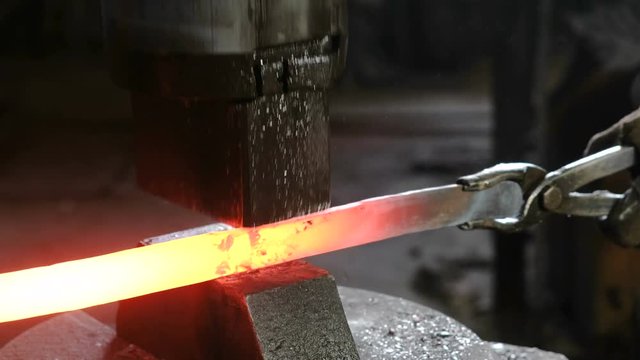 Making the sword out of metal at the forge. Closeup man's hand using pneumatic hammer to shape hot metal.