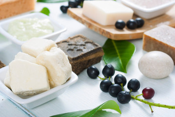 cosmetic clay, soaps, henna blocks, sponge and moisturizer on white wood table