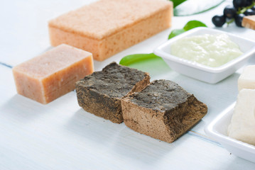 cosmetic clay, soaps, henna blocks, sponge and moisturizer on white wood table