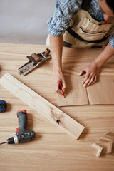 Closeup view of bearded pleasant looking cabinetmaker at the table with pencil making drawing in...