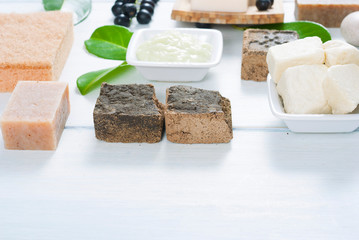 cosmetic clay, soaps, henna blocks, sponge and moisturizer on white wood table