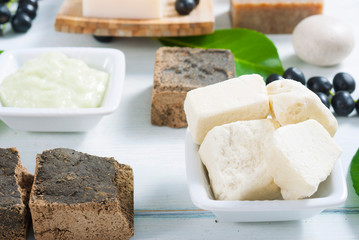 cosmetic clay, soaps, henna blocks, sponge and moisturizer on white wood table