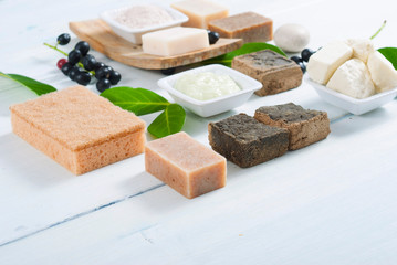 cosmetic clay, soaps, henna blocks, sponge and moisturizer on white wood table