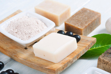 cosmetic clay, soaps, henna blocks, sponge and moisturizer on white wood table