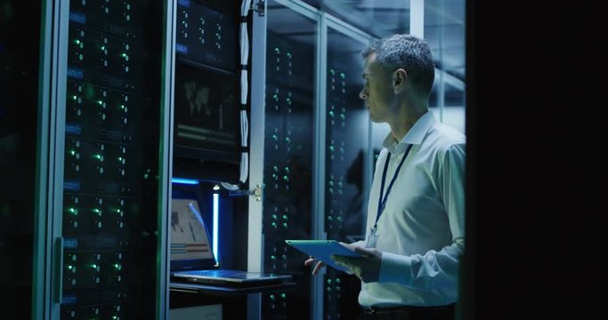 Medium shot of technicians working on a laptop in a data center full of rack servers running diagnostics and maintenance on the system