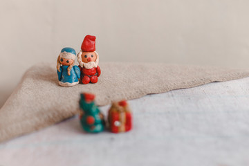 New Year, Santa Claus (Father Frost) and Snow Maiden, Christmas card. Plasticine figurines on a textile linen surface. Foreground out of focus Christmas tree and gift