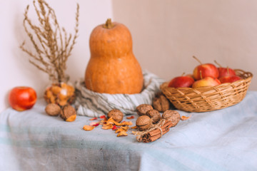 Still life with cinnamon sticks wrapped in twine, pumpkin on a striped linen cloth, apples in a wicker basket stand, walnuts and flower petals in bank. Concept of home comfort in autumn or winter. 