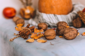 Still life with cinnamon sticks wrapped in twine, pumpkin on a striped linen cloth, apples in a wicker basket stand, walnuts and flower petals in bank. Concept of home comfort in autumn or winter. 